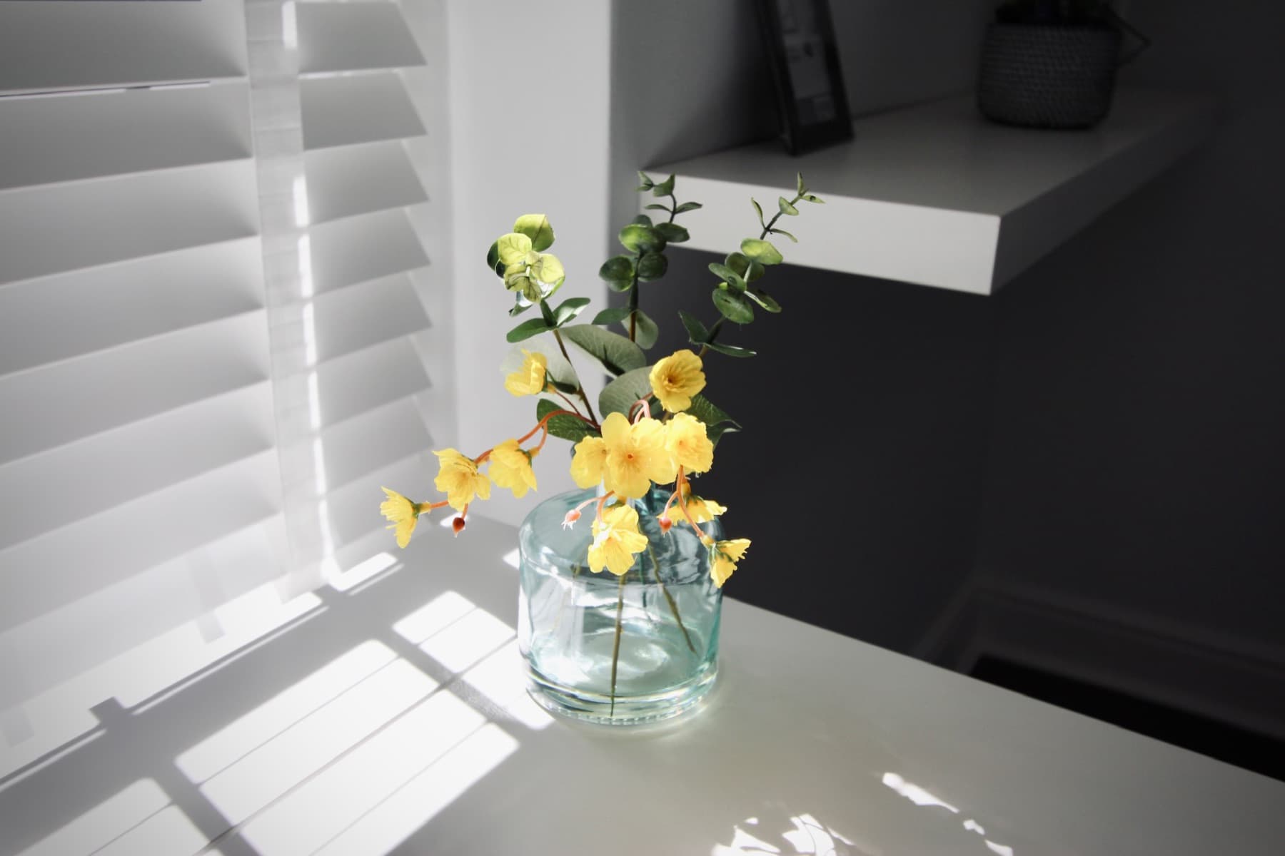 Sunlight through the shutters on fresh flowers at the desk