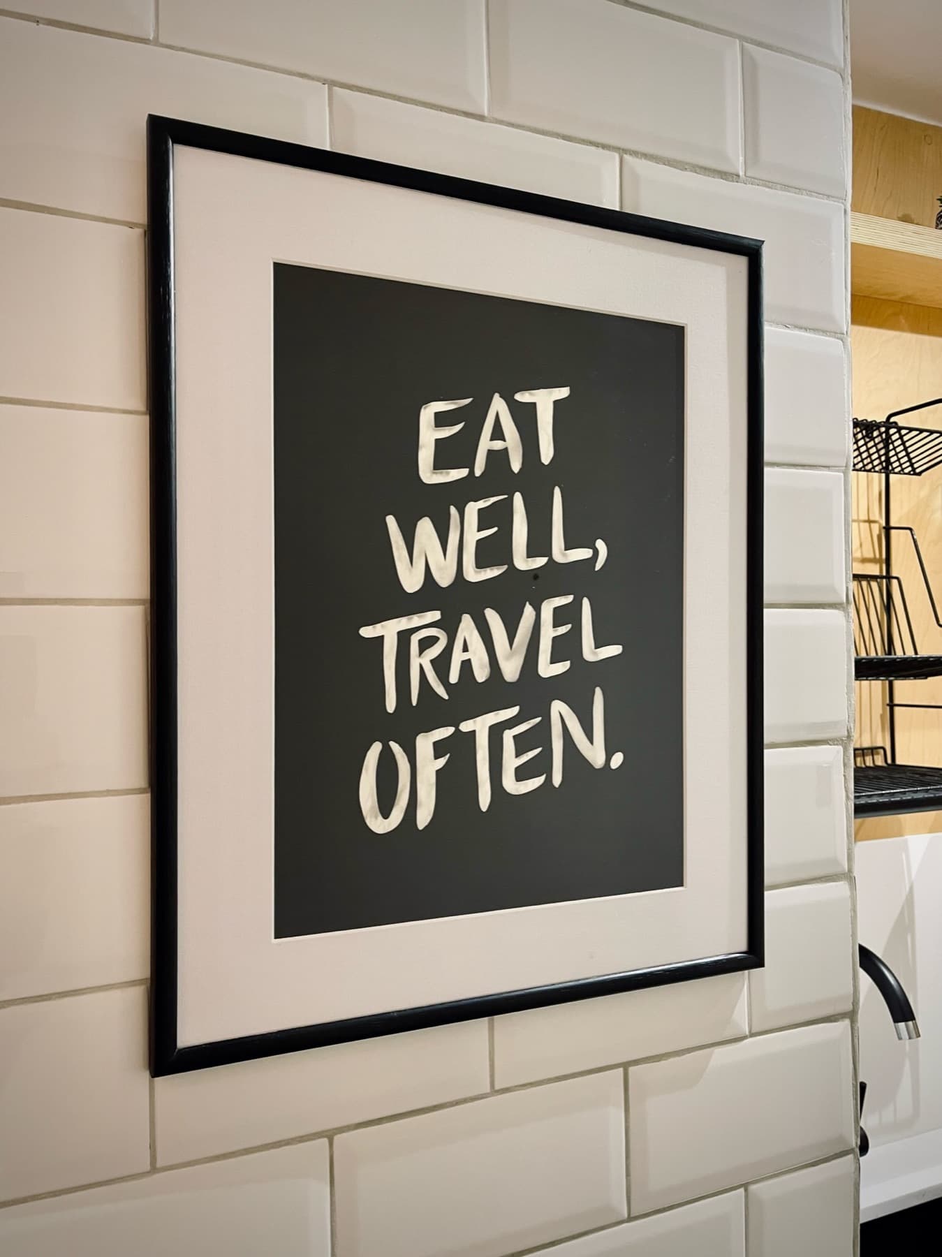 “Eat well, travel often” — framed print against metro tiles